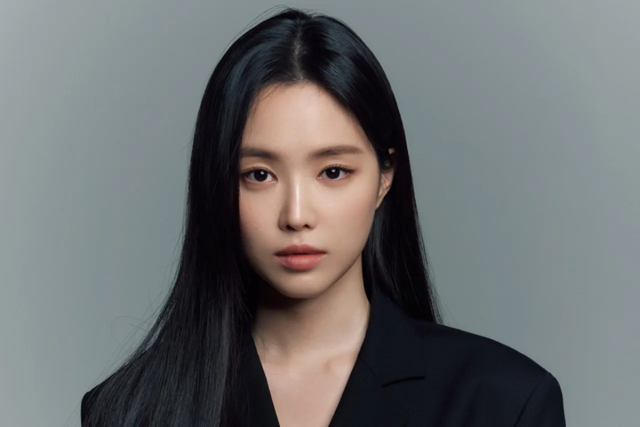 Son Naeun em pose triste, vestindo preto, ao lado de flores brancas em memória da mãe