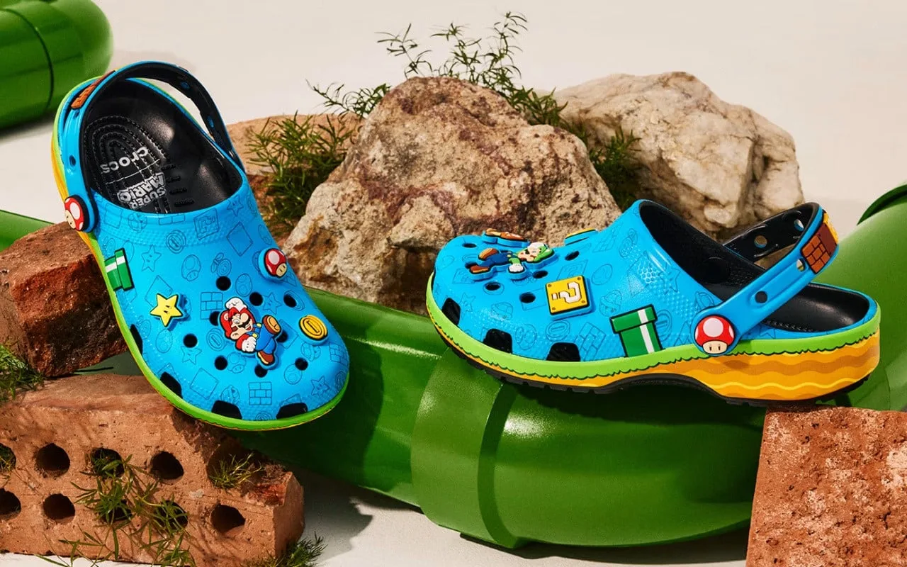 Criança e adulto usando Crocs Super Mario coloridas, correndo na pista de atletismo com bolas de tênis ao fundo