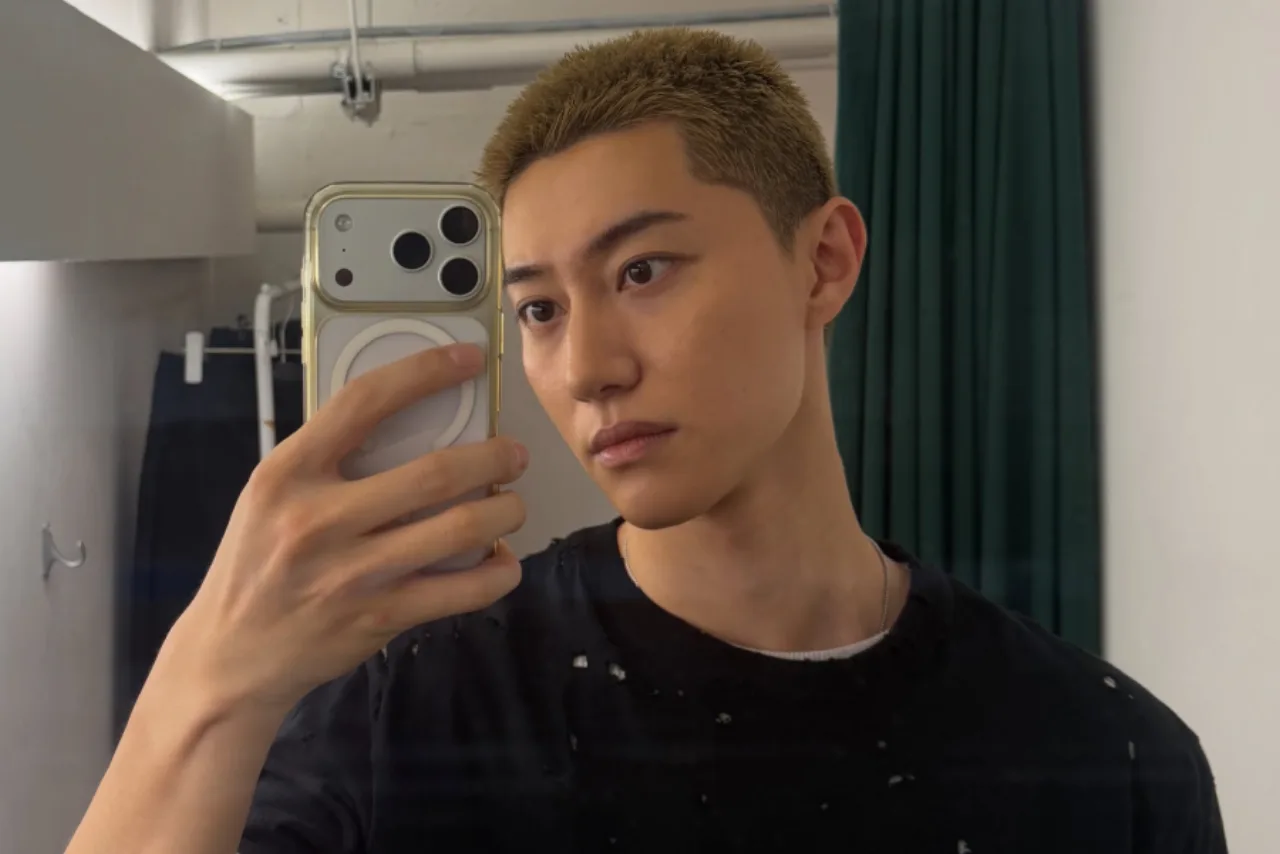 Kwak Dong Yeon em uniforme militar, fazendo flexões ao ar livre ao lado de uma barra de tração e mochila tática