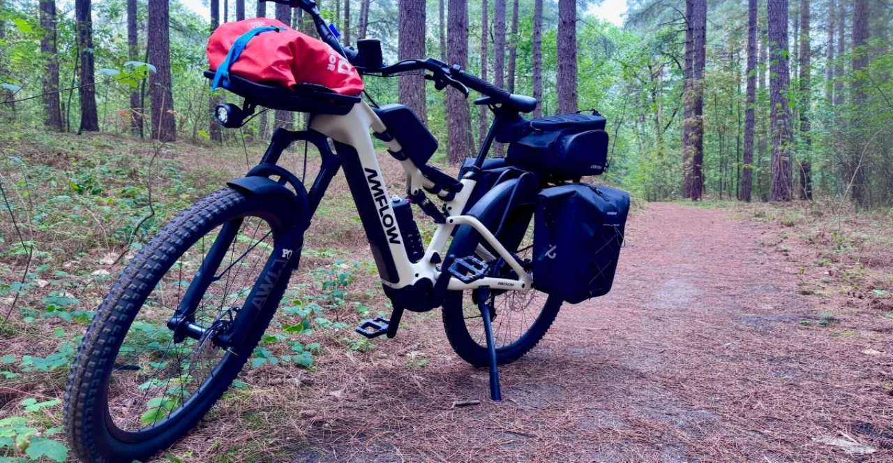 Bicicleta eSUV elétrica com pneus largos, suspensão completa, para-lamas e bagageiro, em fundo urbano e trilha de terra