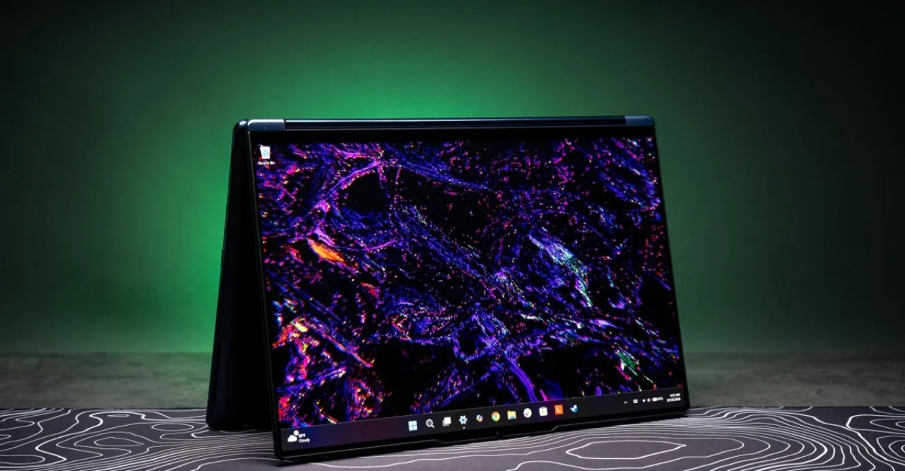 Lenovo Yoga 9n aberto em modo tablet, exibindo tela sensível ao toque com caneta stylus ao lado, ao fundo logo da Apple