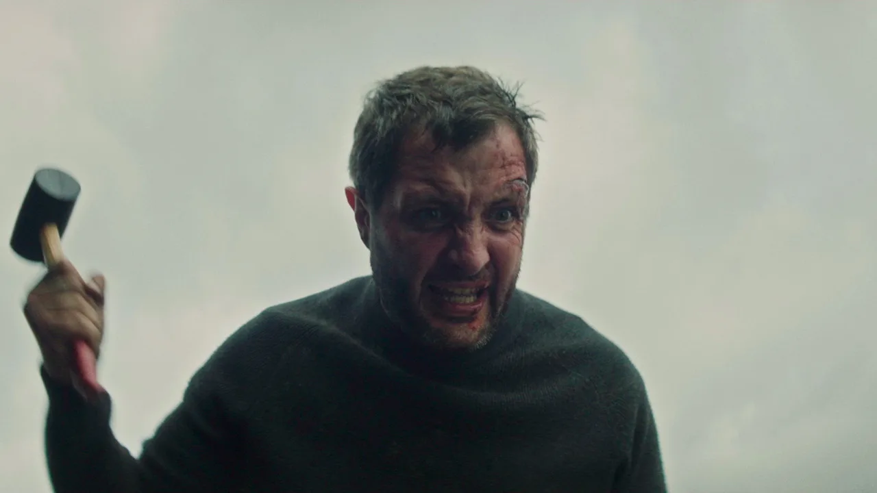 Homem em camiseta preta levantando halteres ao lado de um poster do filme Vincent Must Die