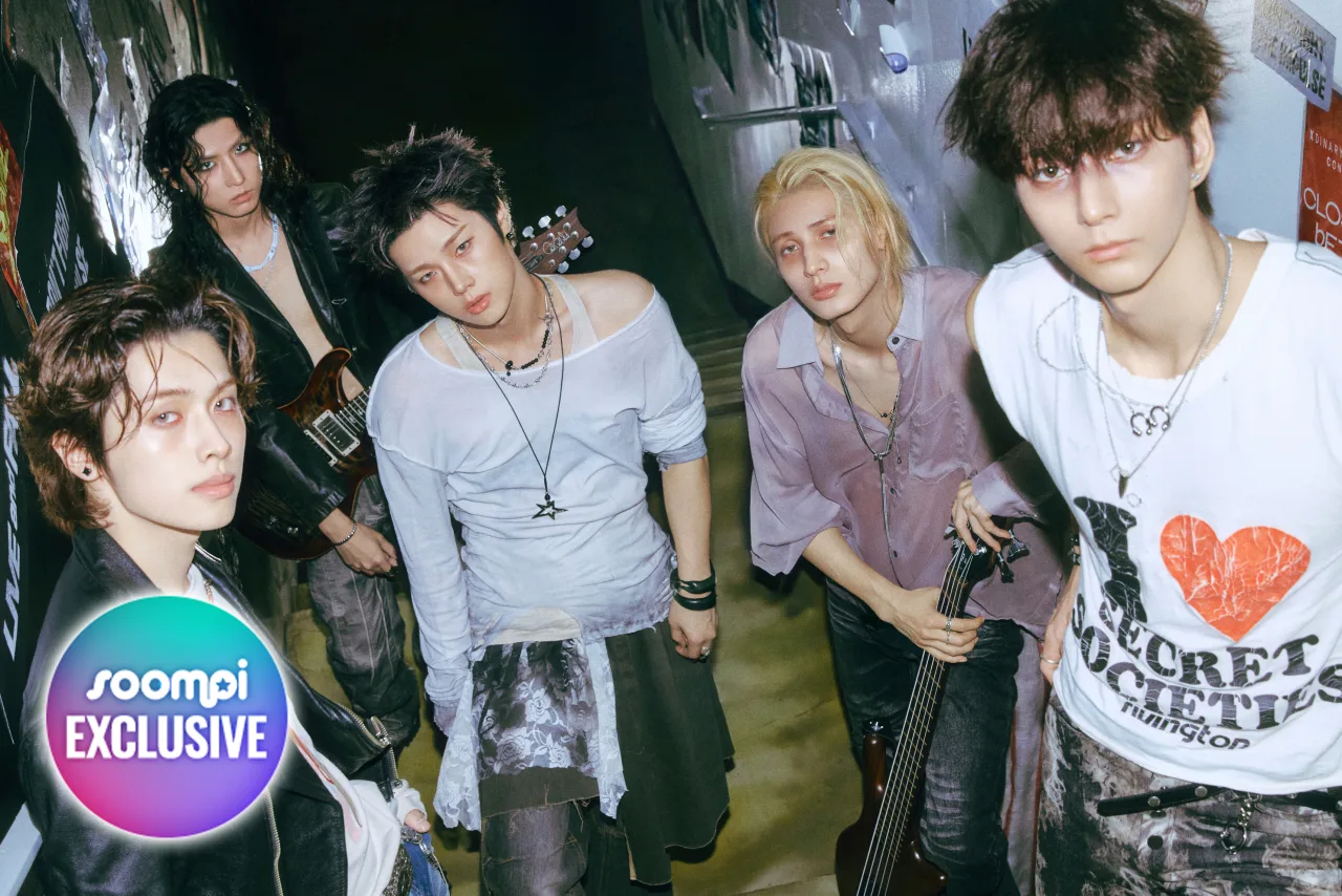 Membros do Xdinary Heroes posam ao lado do CD IMPULSE, com o logotipo da JYP ao fundo