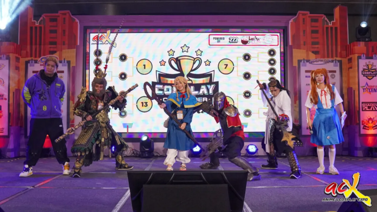Cosplayer em traje de super‑herói, fazendo flexão de braço em palco iluminado, com banners da Expo ao fundo