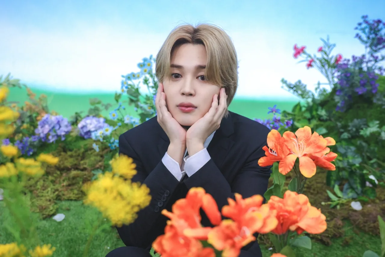 Jimin aparece sorrindo, segurando o selo Platinum da RIAJ ao fundo a bandeira do Japão