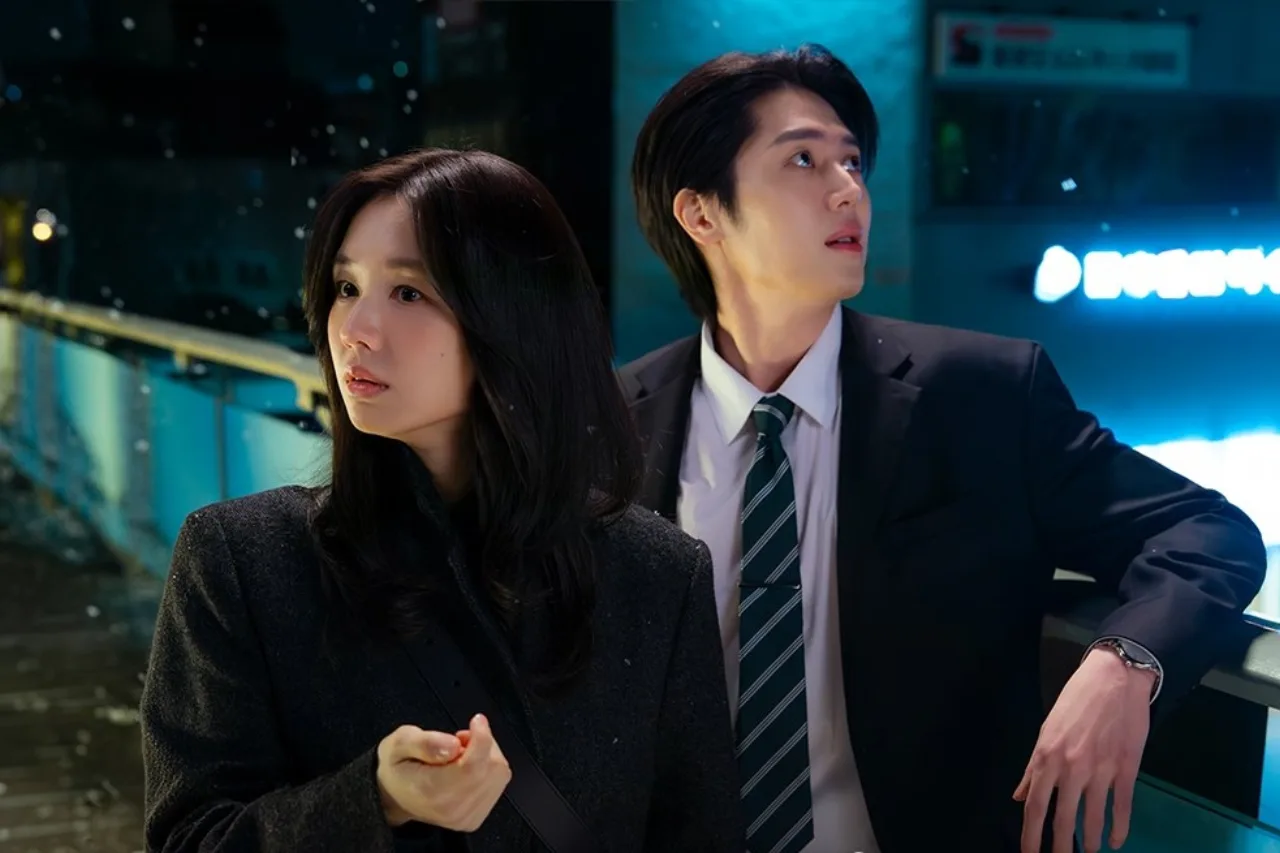 Lee Mi Do e Lee Joo Ahn abraçados na neve, rodeados por flocos e luzes suaves, enquanto Namgoong Ho observa ao fundo