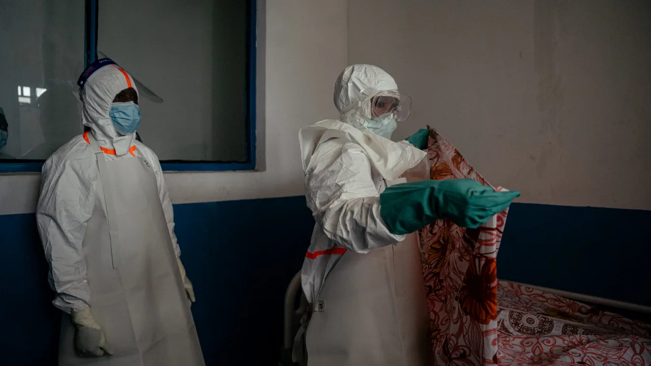 Profissional de saúde com máscara e luvas examinando amostra de sangue em laboratório com equipamentos de proteção