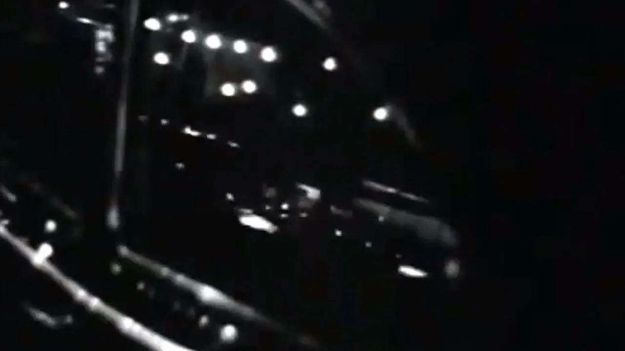 Jovem faz agachamento segurando halteres ao lado de um pequeno robô azul brilhante, lembrando H.E.R.B.I.E