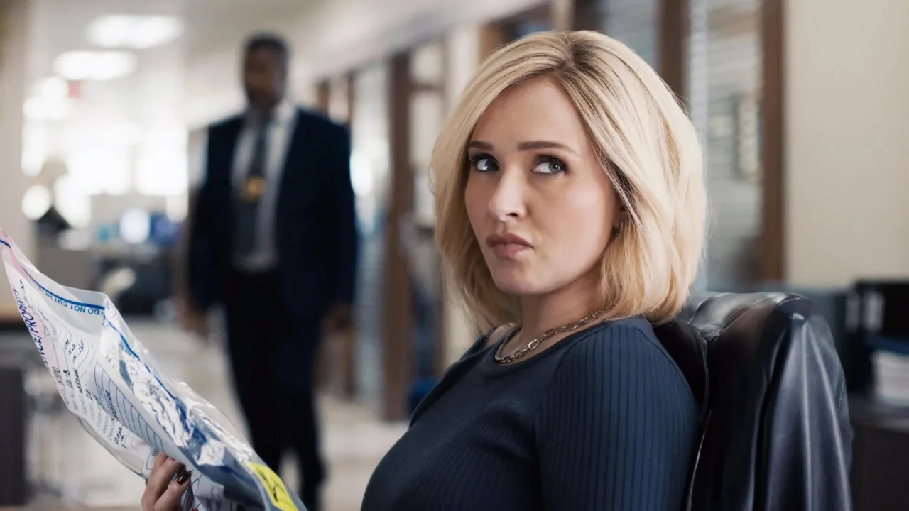 Hayden Panettiere em roupa esportiva, segurando halteres, sobre um tapete de yoga com garrafa d’água ao lado