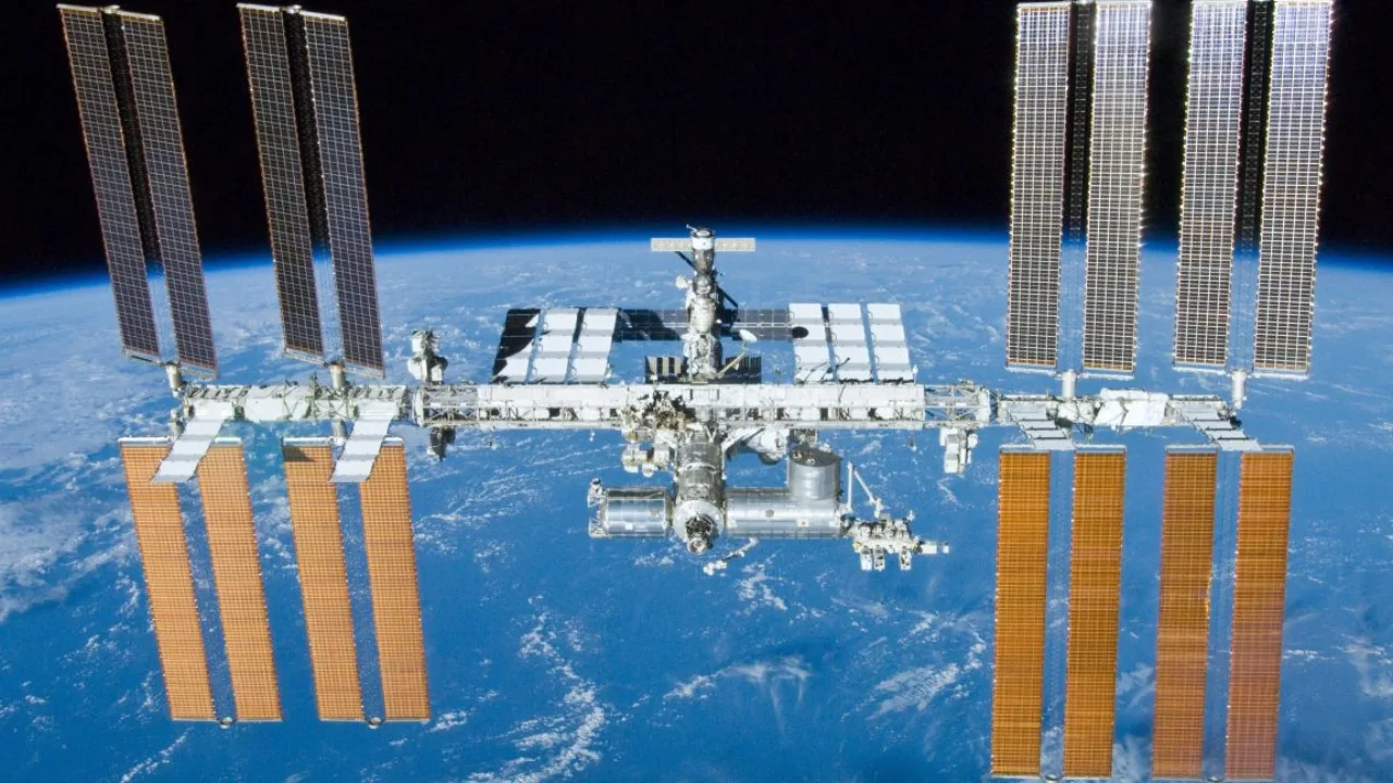 Astronauta realiza exercício em ergômetro próximo a painéis de controle e cabos no interior da estação espacial