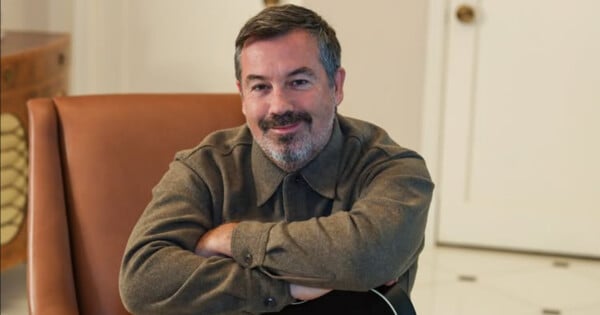 Duncan Sheik em close, com fundo de cartaz de Spring Awakening e notas musicais
