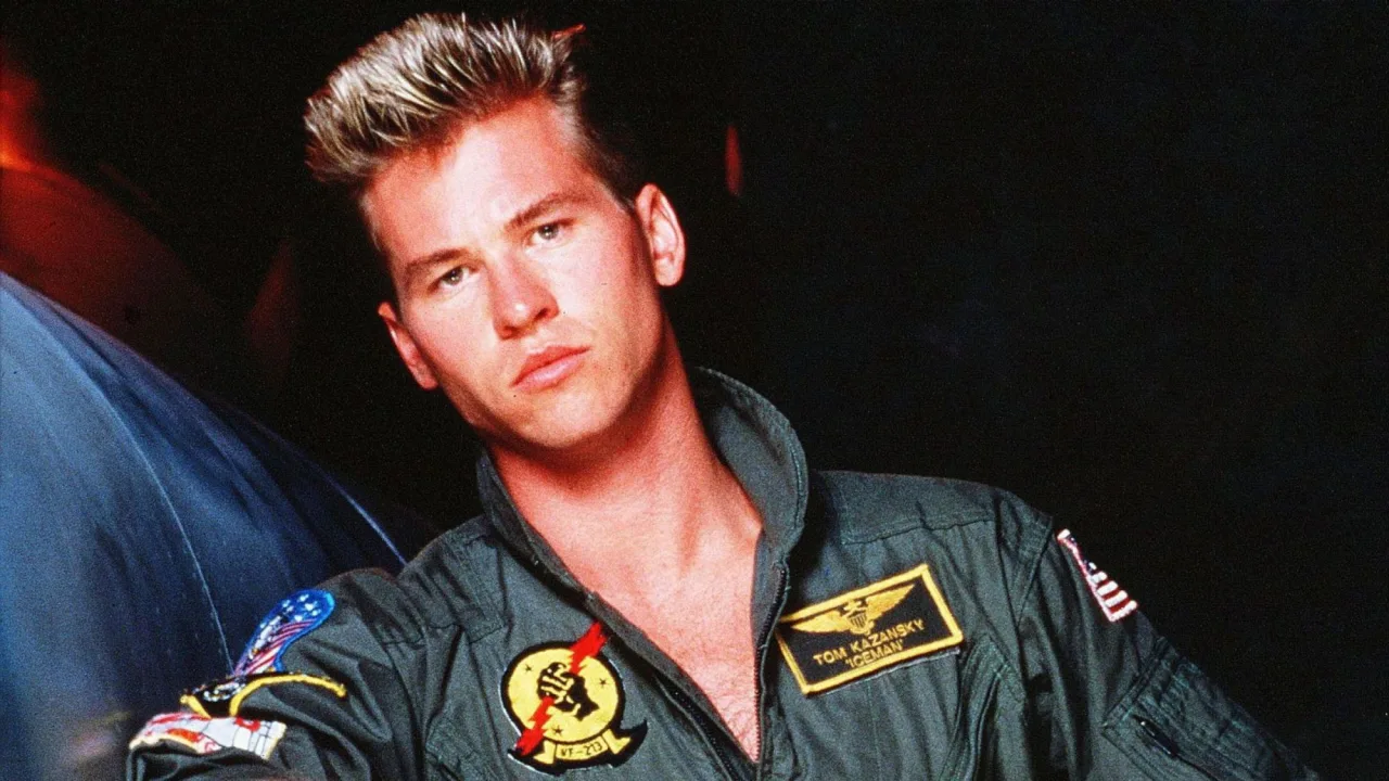 Capacete Iceman de Top Gun, com máscara de oxigênio e mangueiras, sobre fundo escuro ao lado do logotipo do filme
