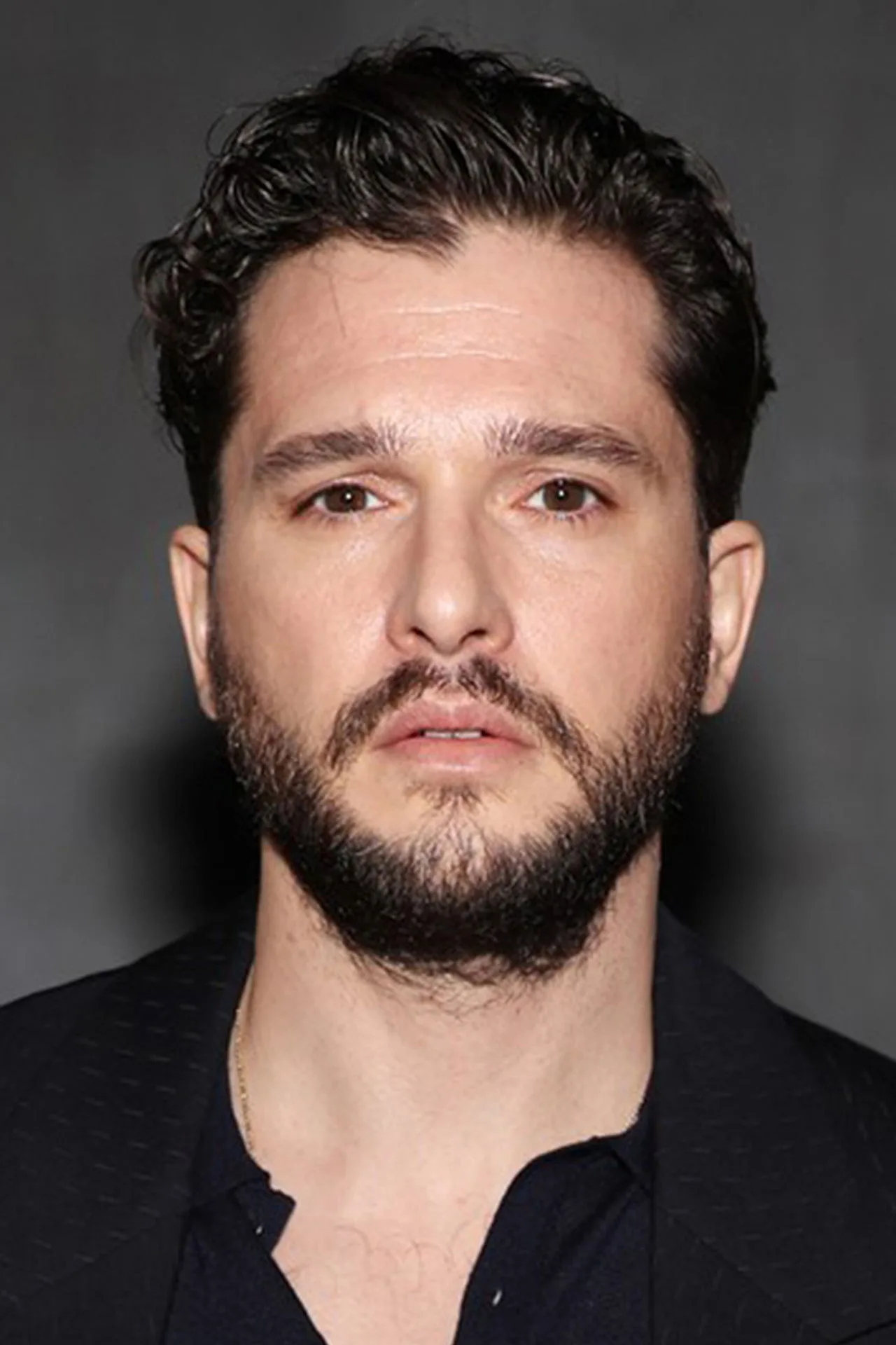 Kit Harington faz flexão de braço em academia, usando camiseta preta, com halteres e garrafa de água ao fundo