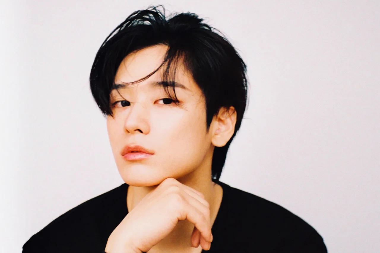 Juyeon vestindo roupa de academia, segurando halteres, ao fundo um espelho e tapete de yoga