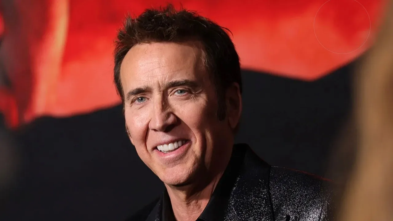 Mascara de teia vermelha sobre fundo preto ao lado de uma caneca de café com o rosto de Nicolas Cage