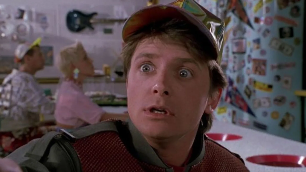 Um colecionador levanta peso enquanto exibe o pôster enrolado de Back to the Future sobre um rack de halteres