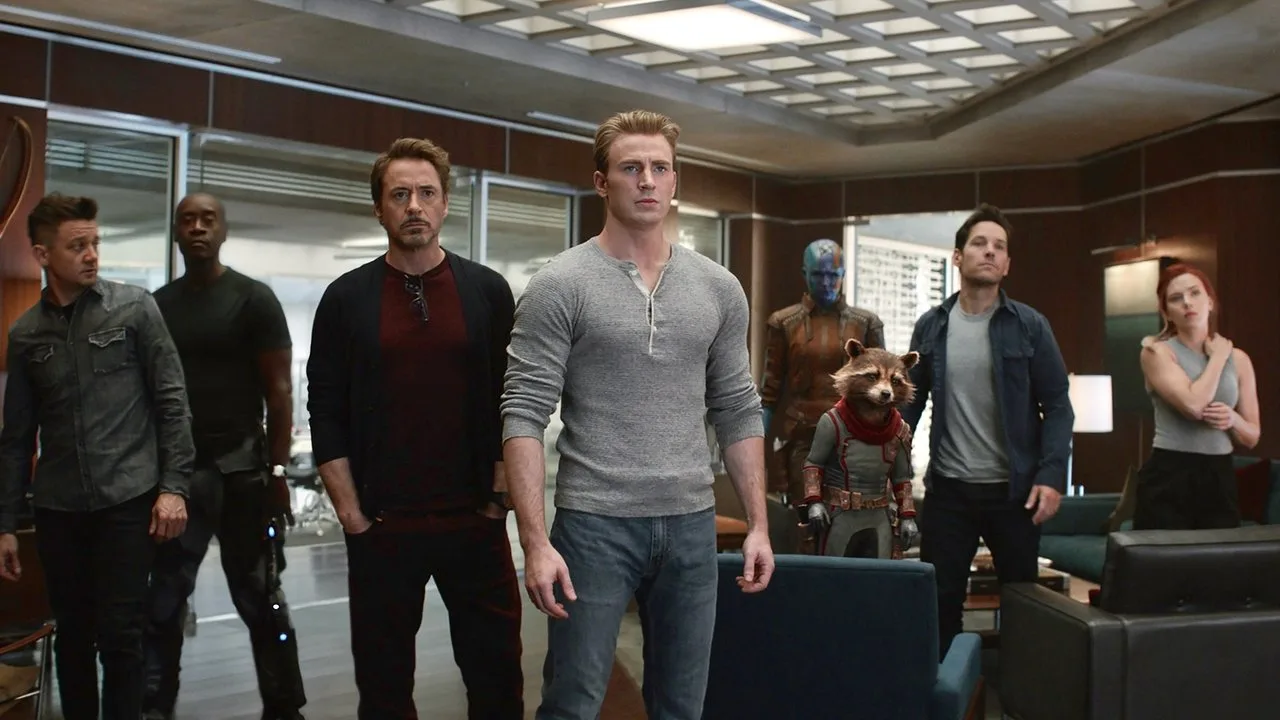 Homem musculoso fazendo flexão ao lado de pôster da capa de Avengers: Endgame, segurando halteres
