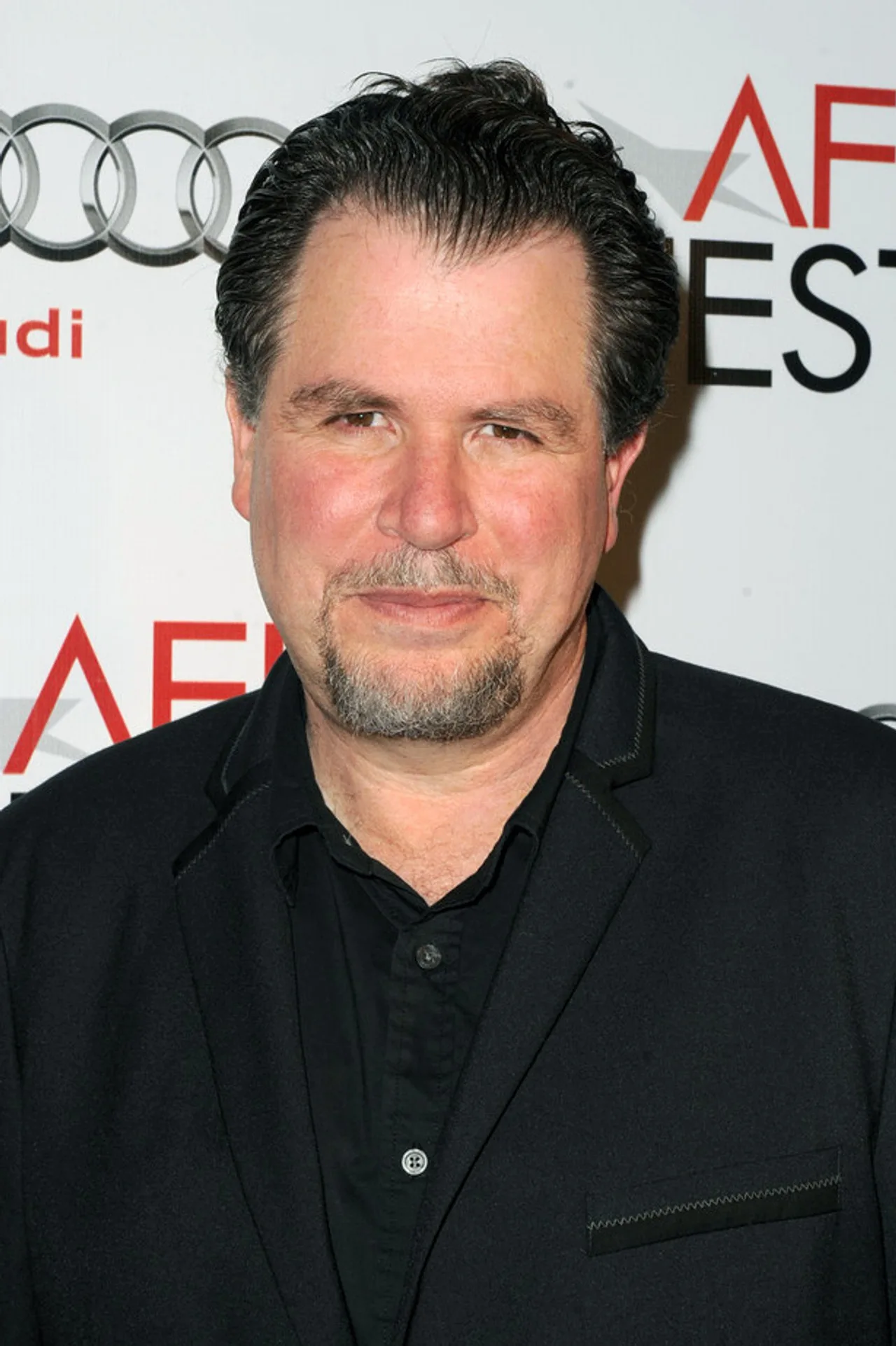 Homem vestindo camiseta de The Beastmaster levanta halteres ao lado de TV exibindo cena do filme