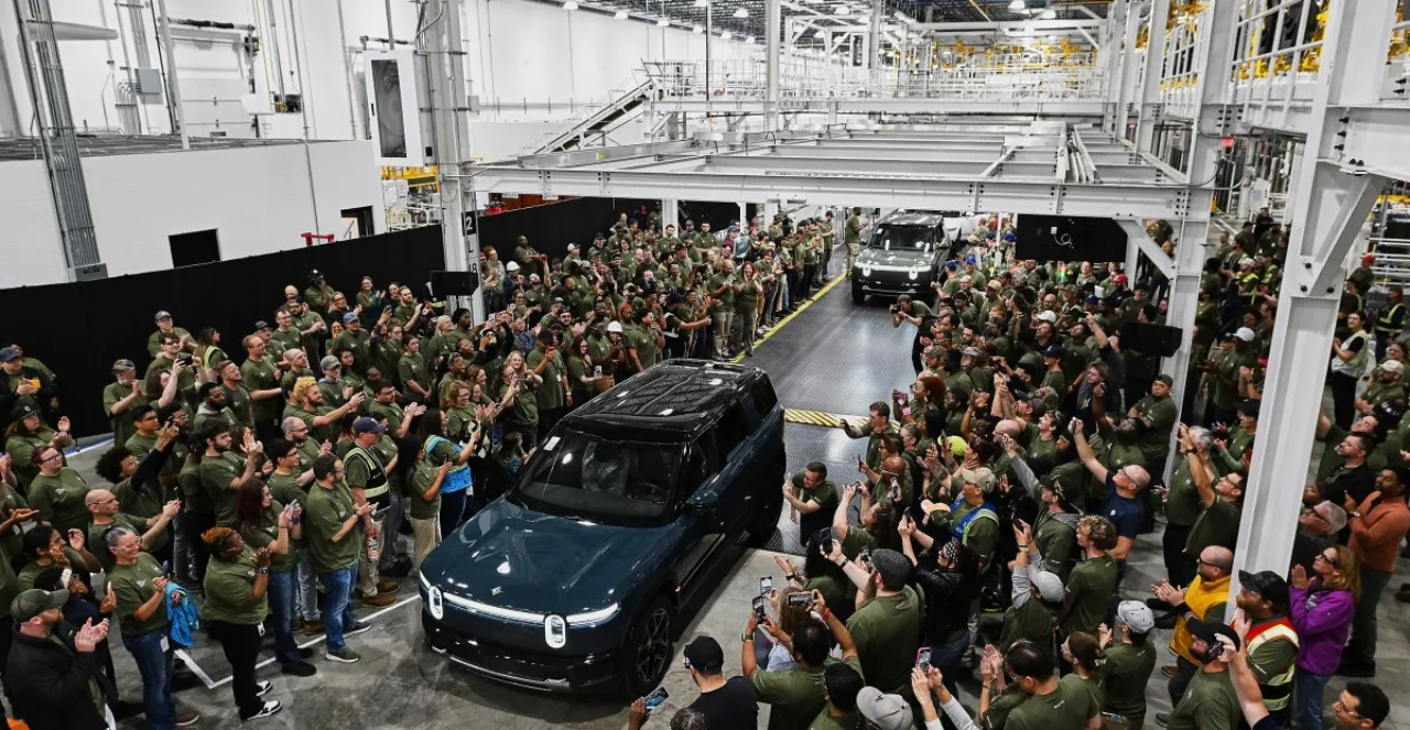 Mulher fazendo agachamento segurando bateria de carro elétrico ao lado de um Rivian