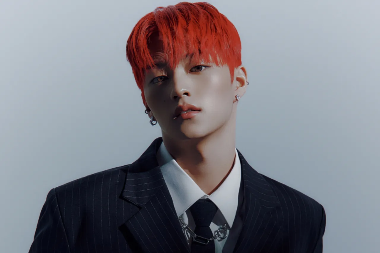 Choi Woojin aparece de perfil, olhar melancólico, vestindo jaqueta preta, ao lado do logotipo do TIOT