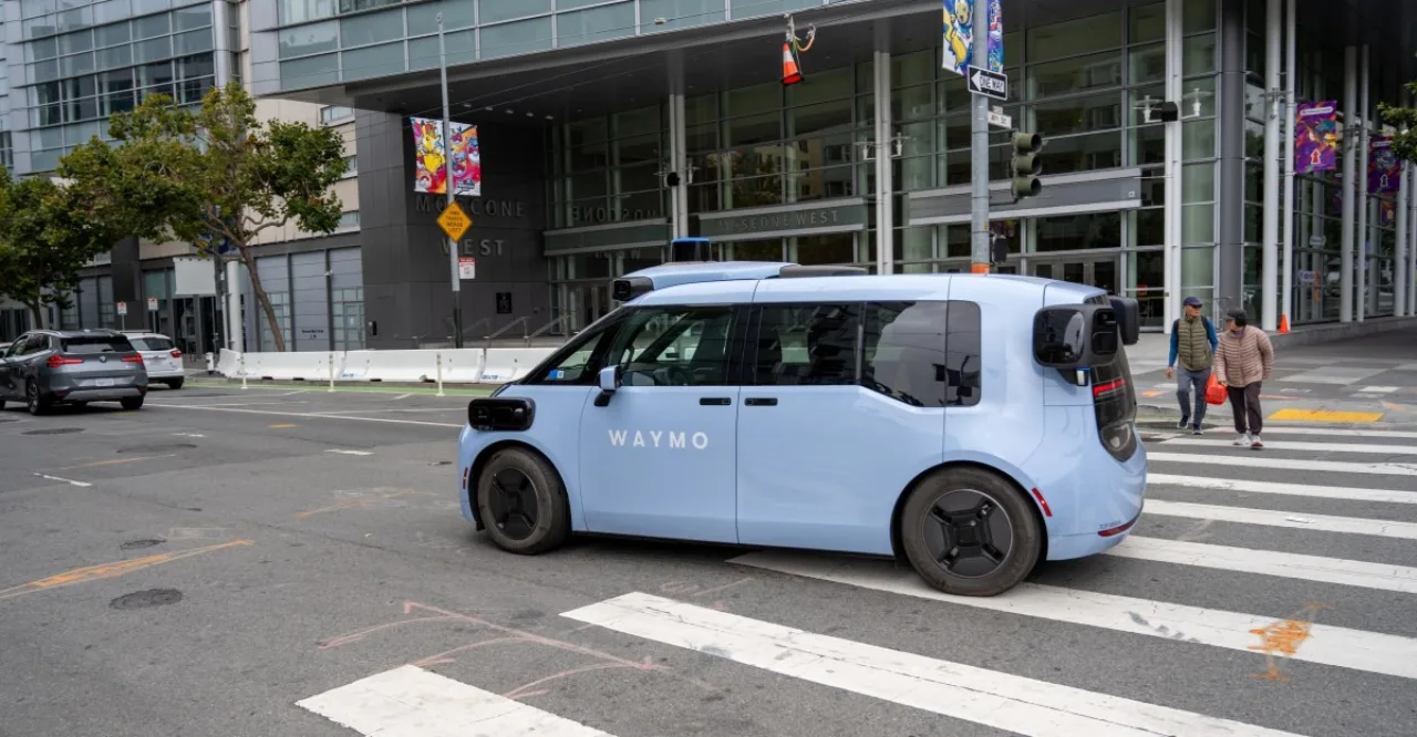 Um robotáxi Waymo estacionado ao lado de um ponto de ônibus, com o logotipo da Visa exibido na lateral do carro