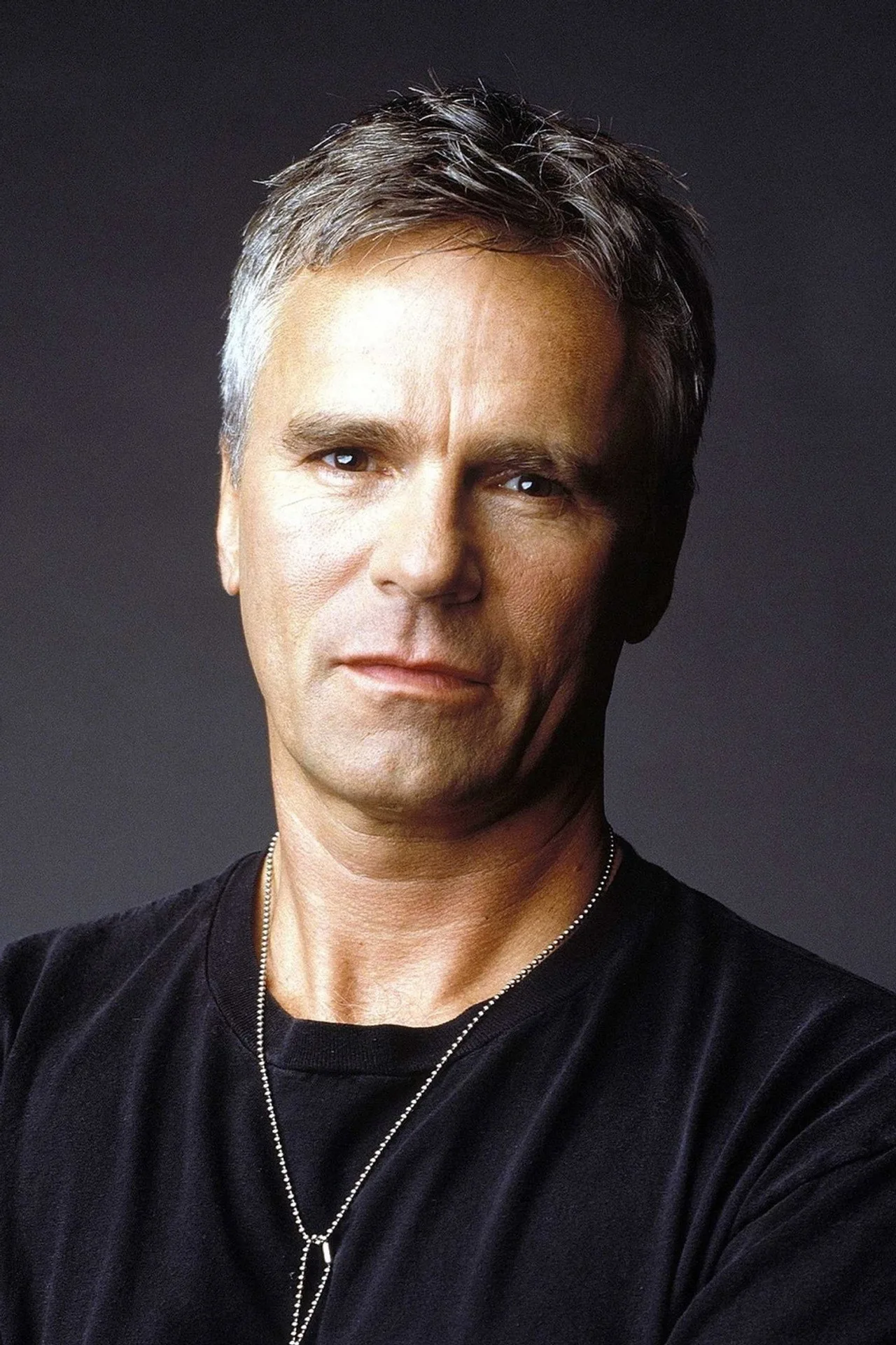 Homem musculoso vestindo camiseta de Stargate SG‑1 faz flexão ao lado de um poster da série