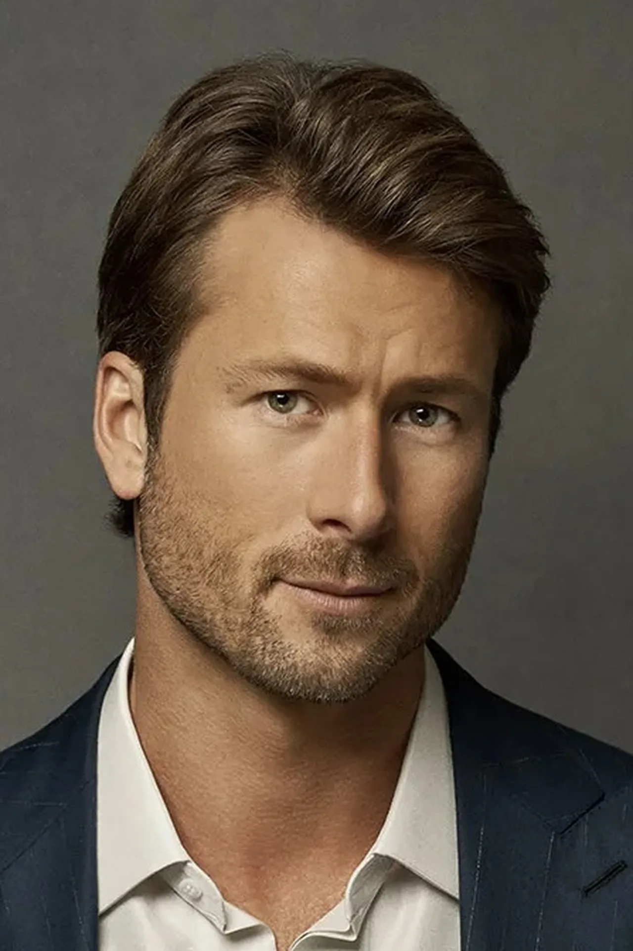 Glen Powell levanta barra de ferro na academia, vestindo camiseta vermelha e mostrando músculos definidos