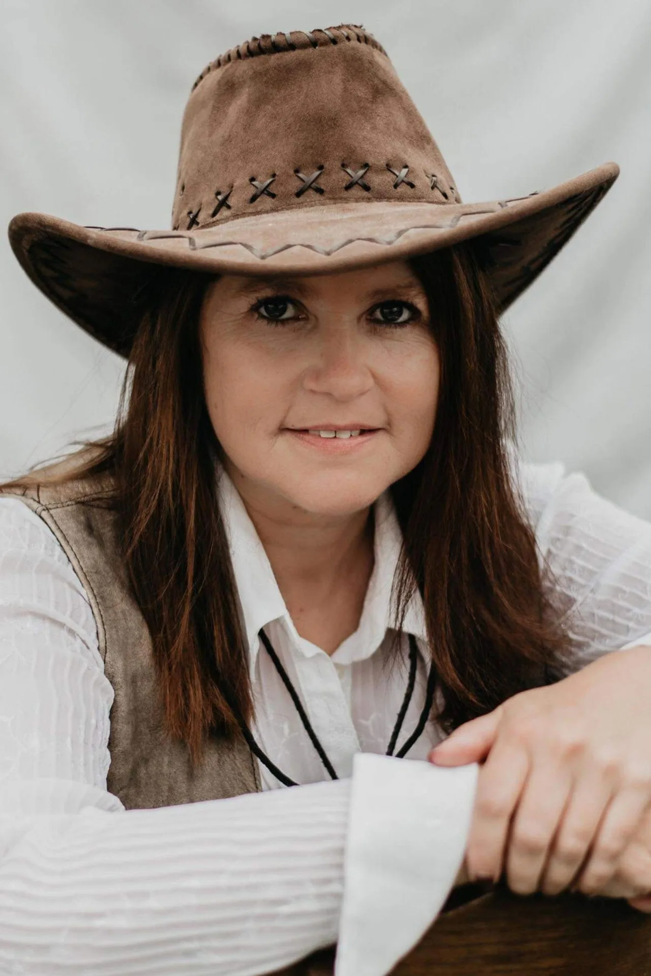 Mulher em jaqueta de pele faz agachamento com kettlebell em forma de revólver sobre neve, usando chapéu de cowboy