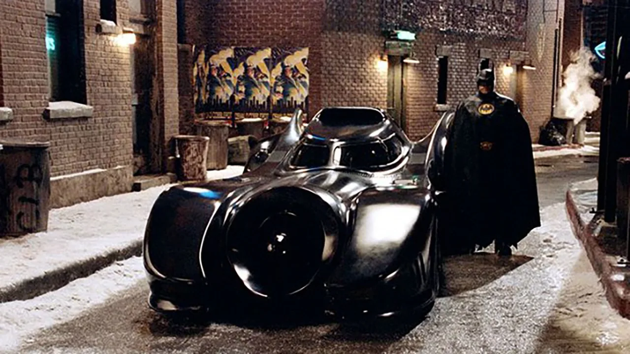 Batmobile de Batman Returns, com faróis vermelhos, sobre fundo escuro ao lado do logo da Julien’s Auctions