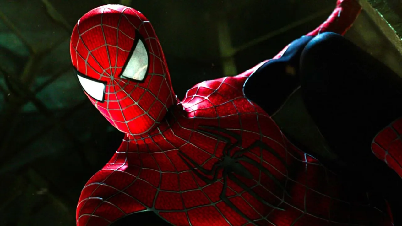 Homem musculoso fazendo flexões, vestindo o traje vermelho e dourado de Homem-Aranha, ao lado de halteres e uma garrafa d'água