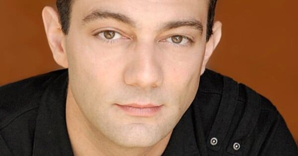 Mike McFarland sorrindo ao microfone, com logos de Dragon Ball Z e One Piece ao fundo